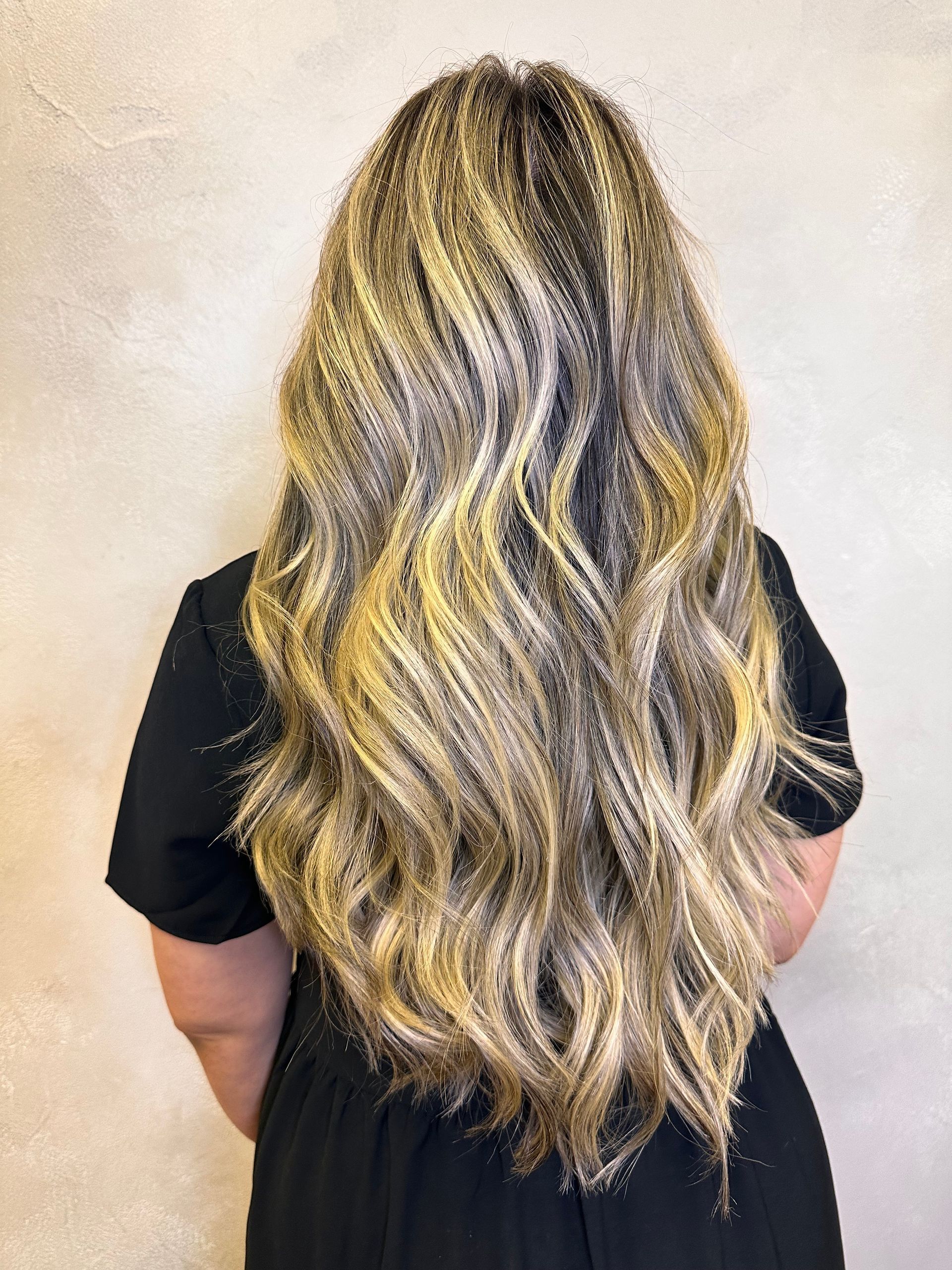 A woman with long blonde hair is wearing a black dress.