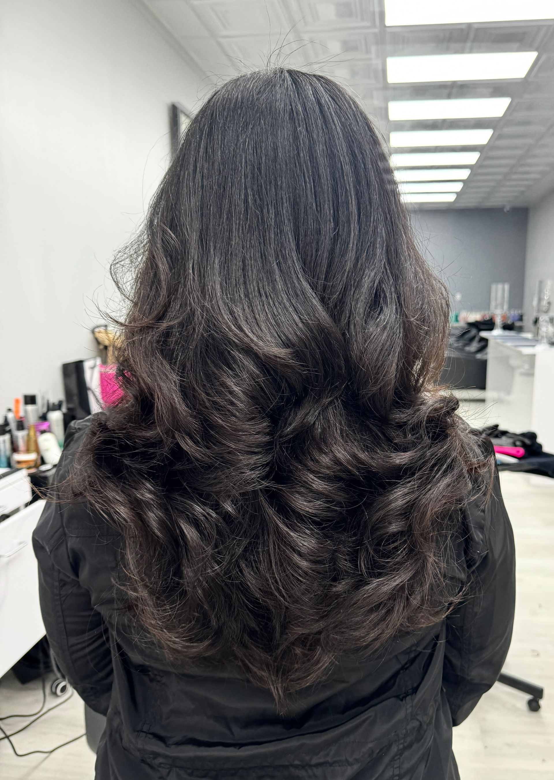 A woman with long black hair is standing in a salon.
