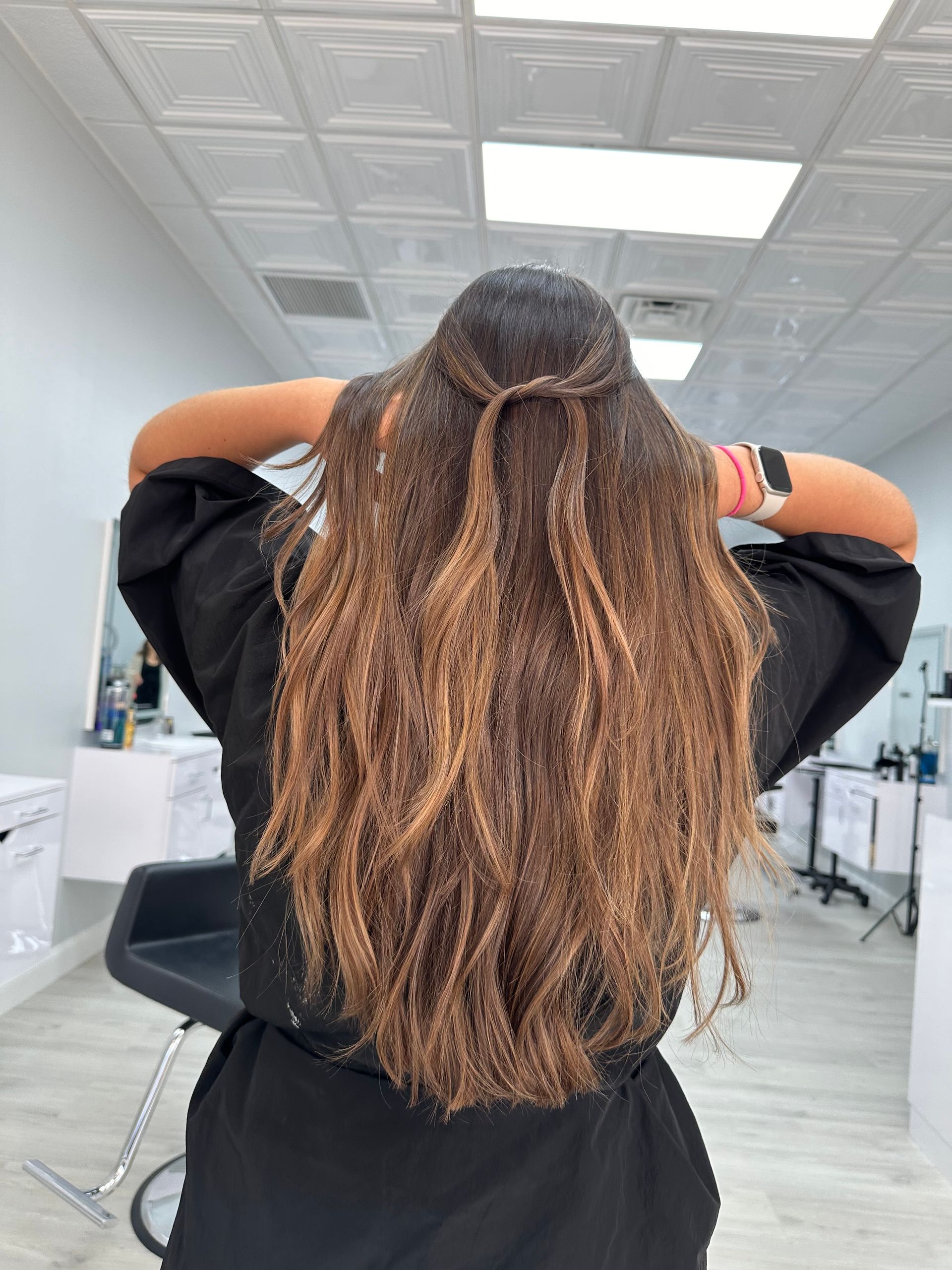 A woman with long hair is standing in a salon with her hands in her hair.