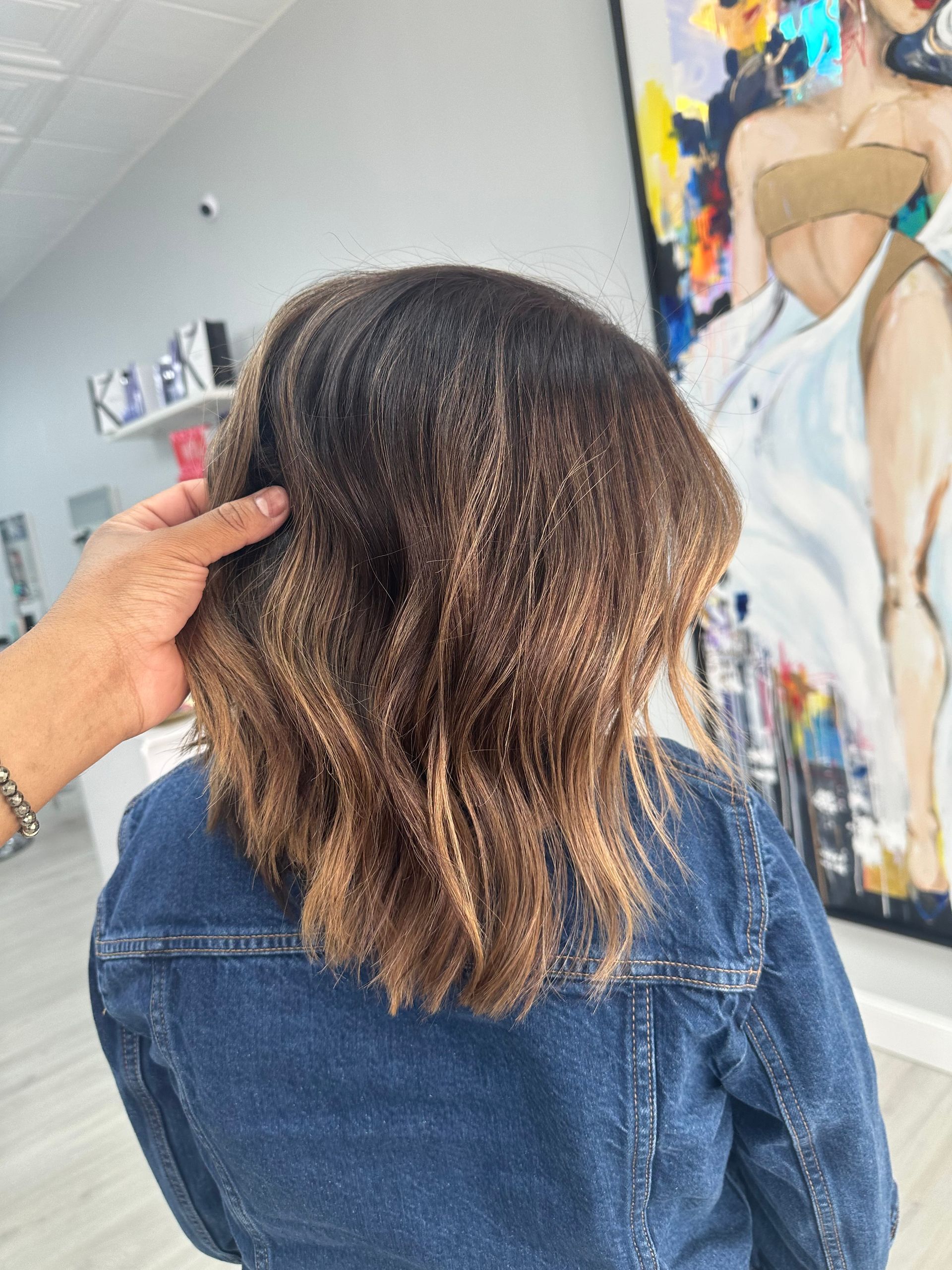 A woman in a denim jacket is getting her hair done in a salon.
