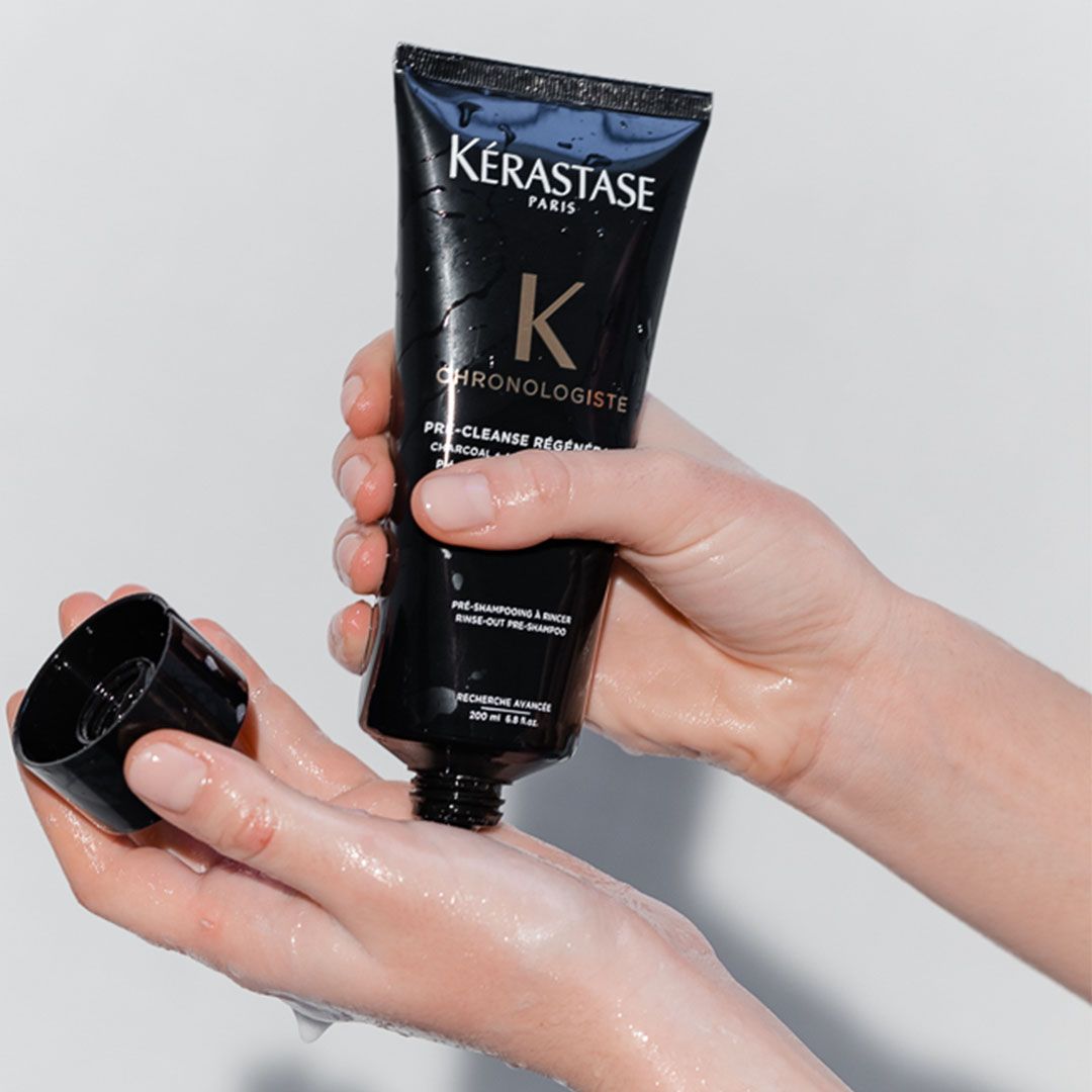 A person is holding a bottle of Kérastase shampoo in their hands