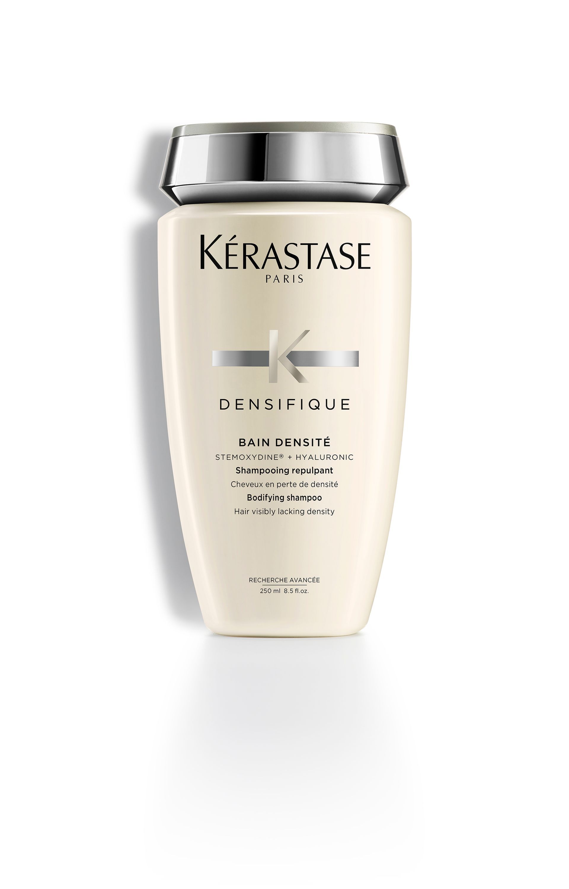 A bottle of Kérastase Densifique shampoo on a white surface.