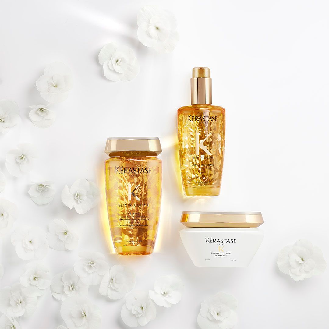 Three bottles of hair products are sitting on top of each other on a table surrounded by white flowers