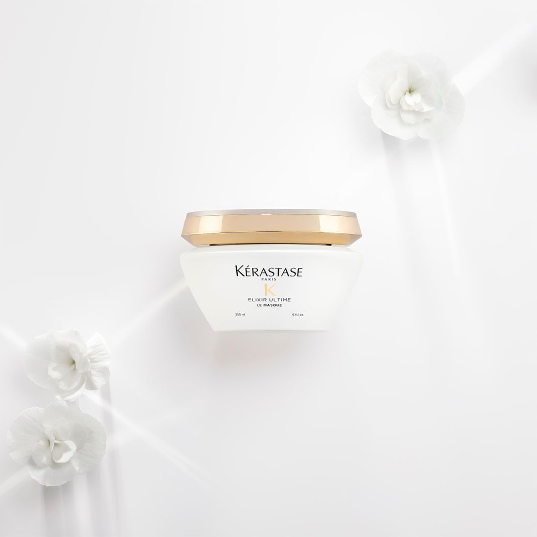 A white container with a gold lid is sitting on a white surface surrounded by white flowers
