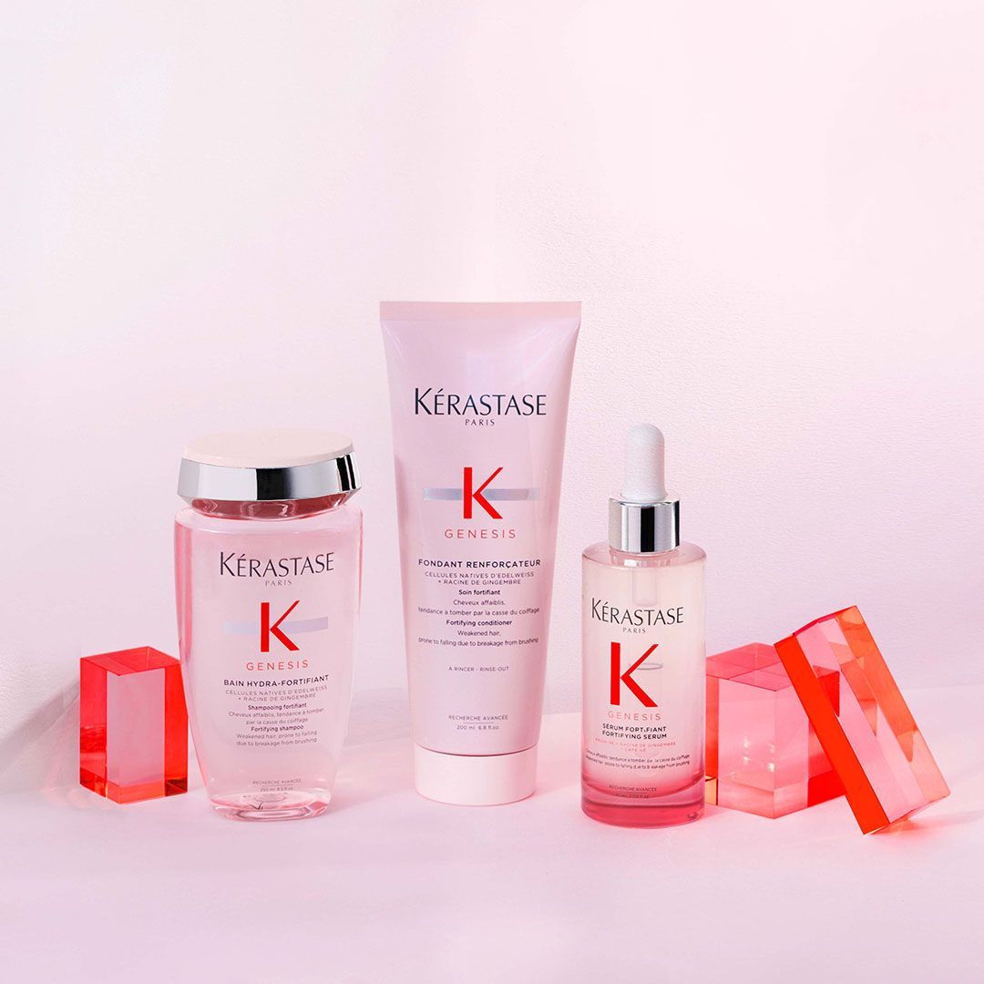 Three bottles of Kérastase hair products are sitting on a pink table