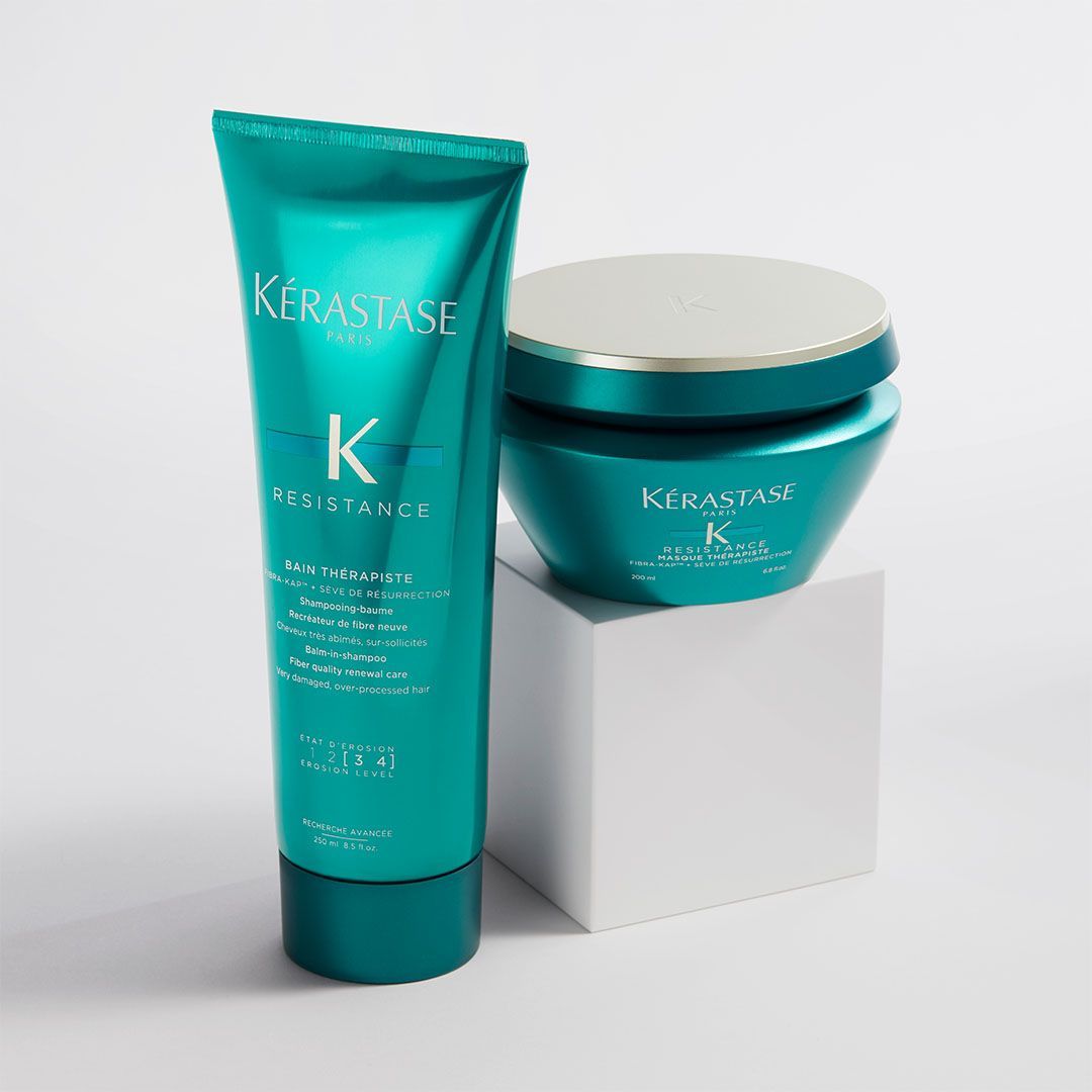 Two bottles of Kérastase hair products are sitting on a white cube