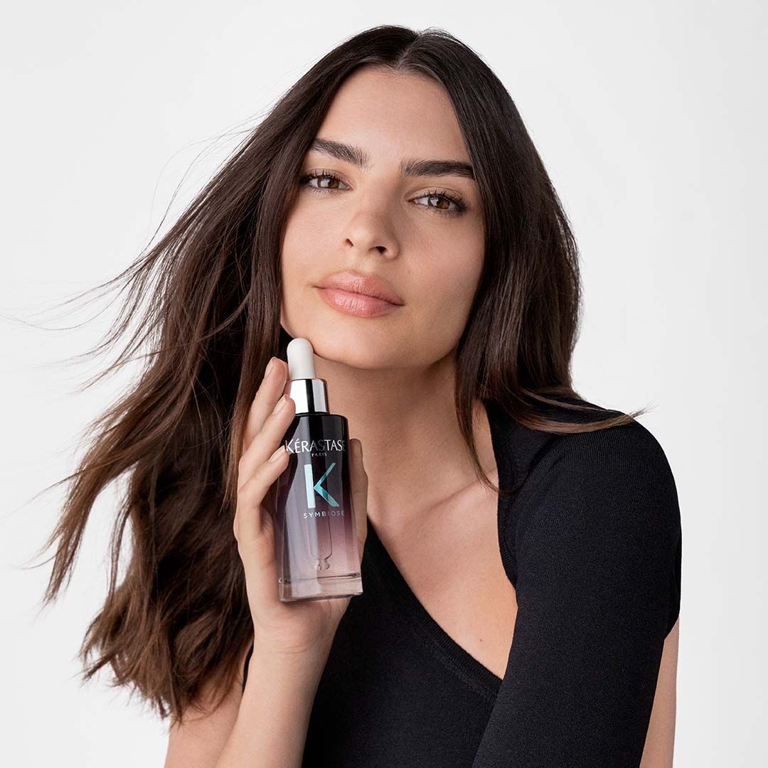 A woman in a black top is holding a bottle of hair product