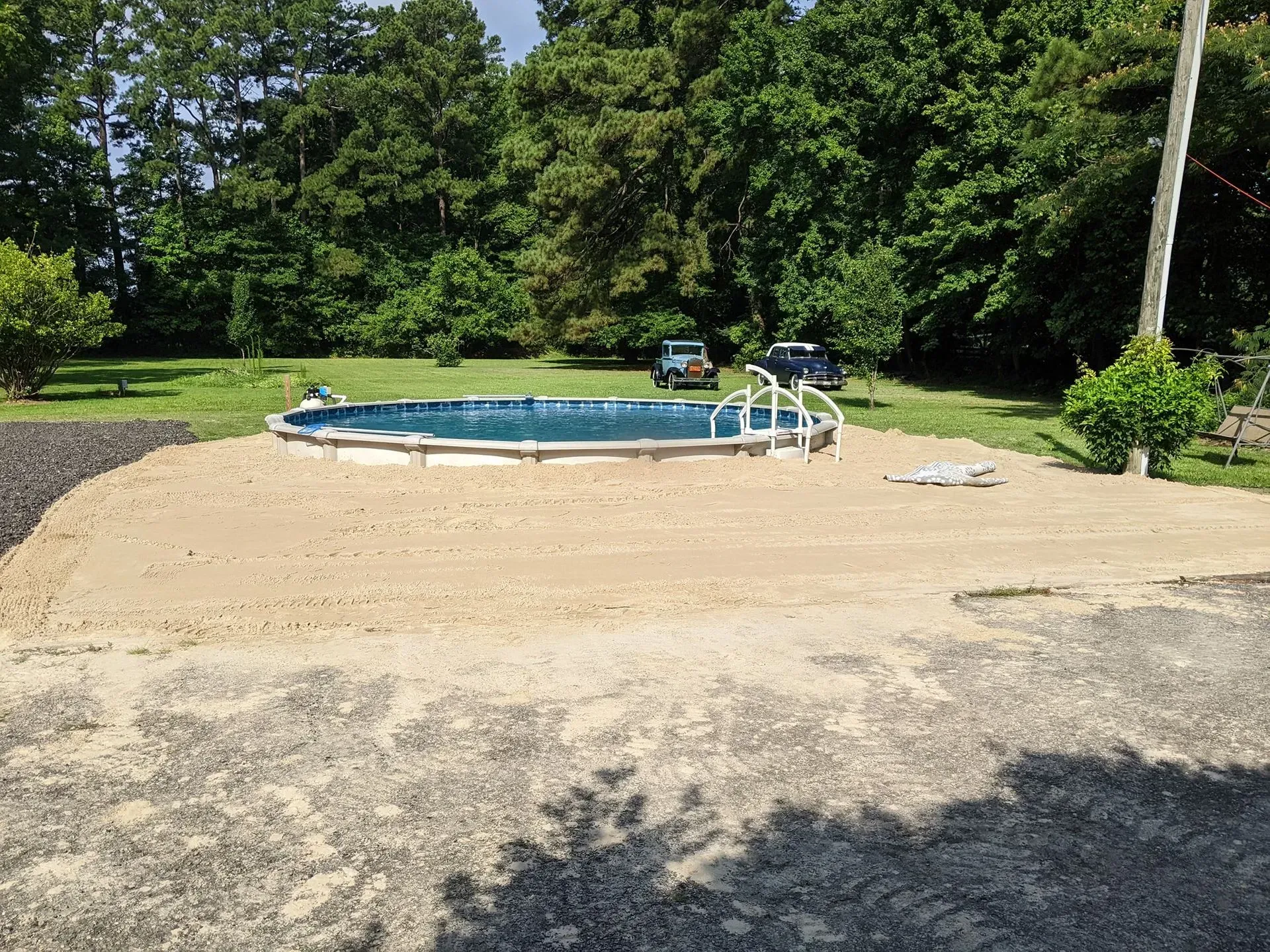 Oval above-ground pool on a gravel pad, with trees and lawn in the background