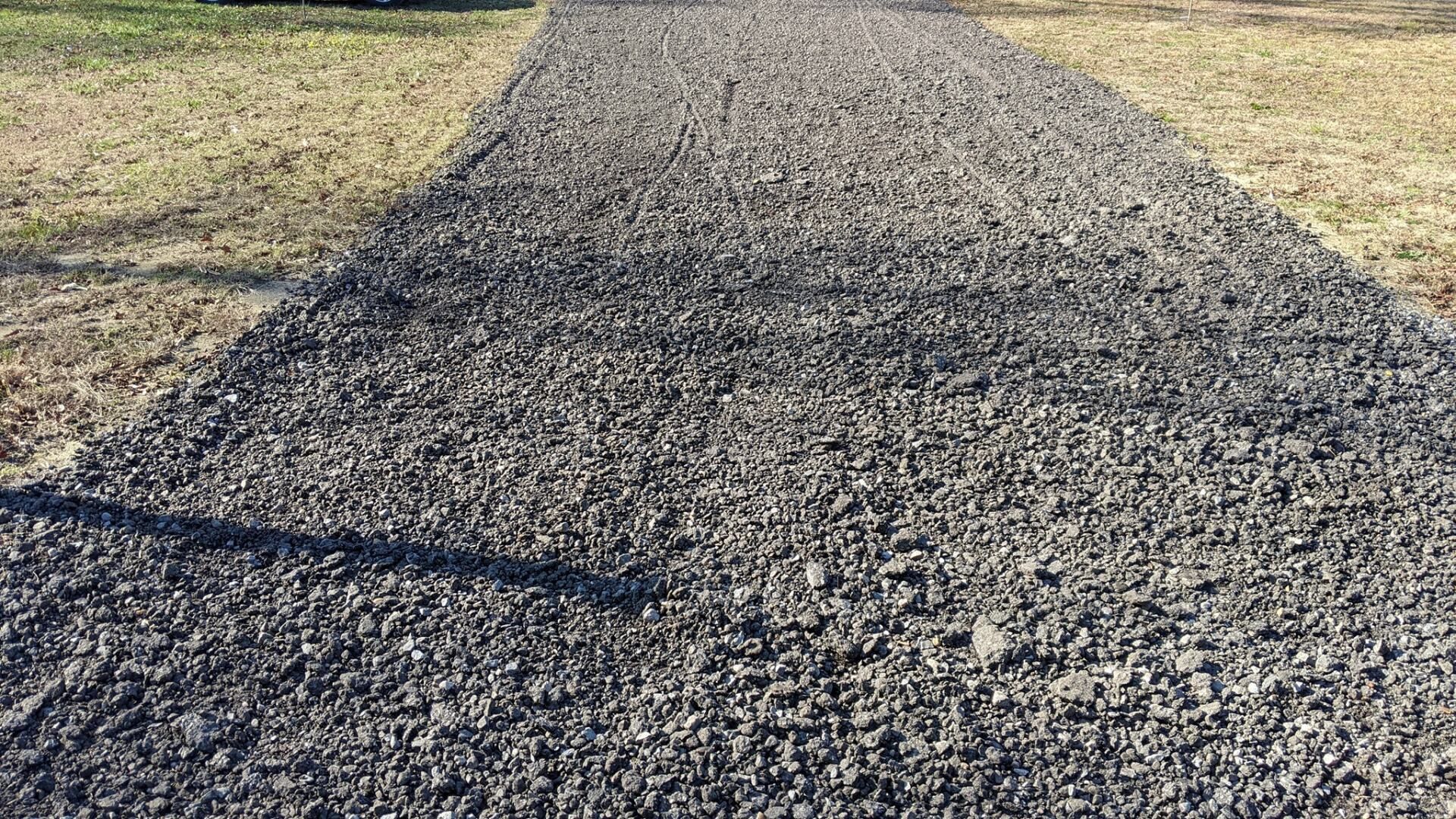 Gravel path stretching into the distance through grassy fields under bright daylight