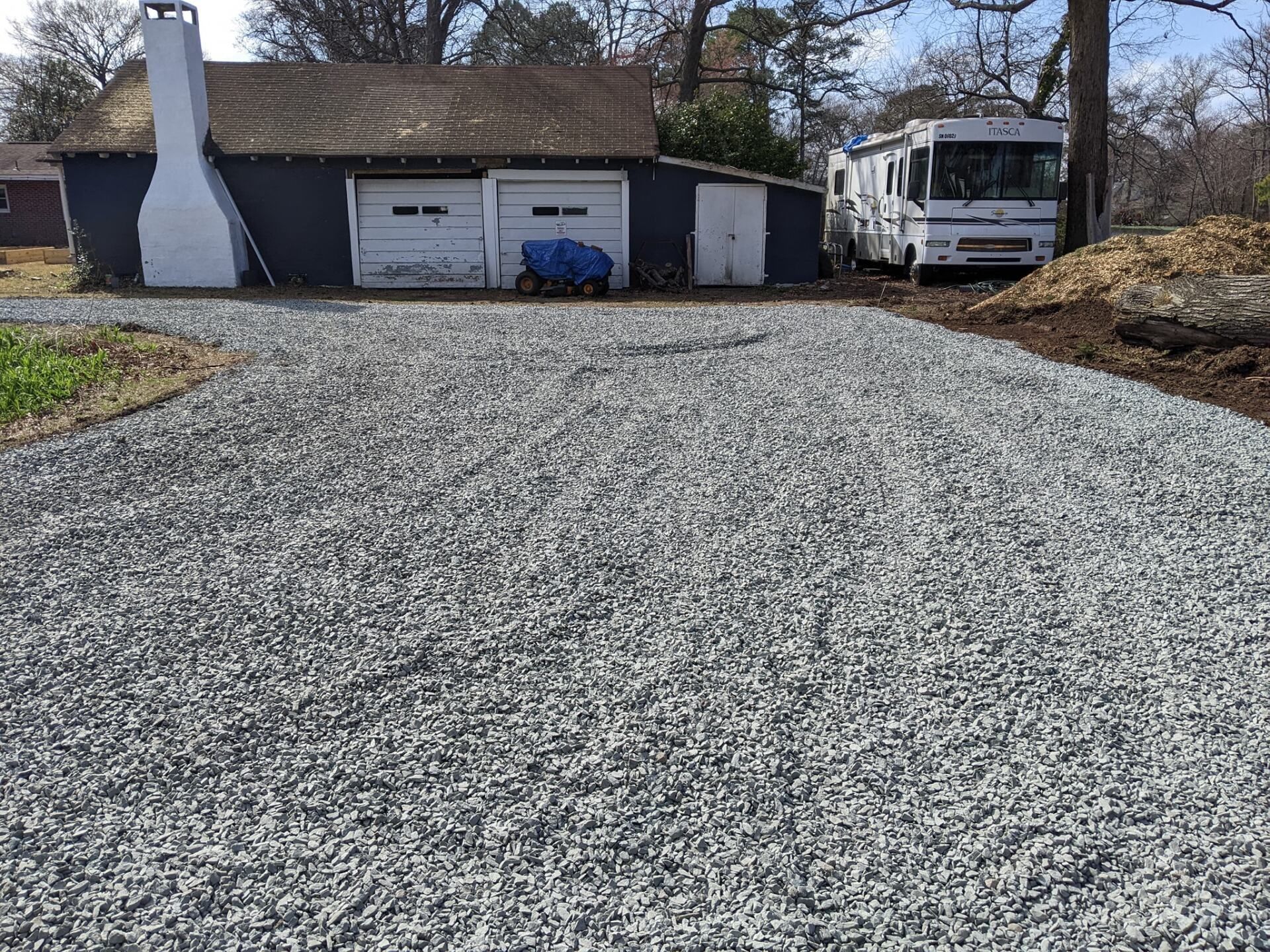 Gravel driveway leading to a garage and RV beside a house on a sunny day