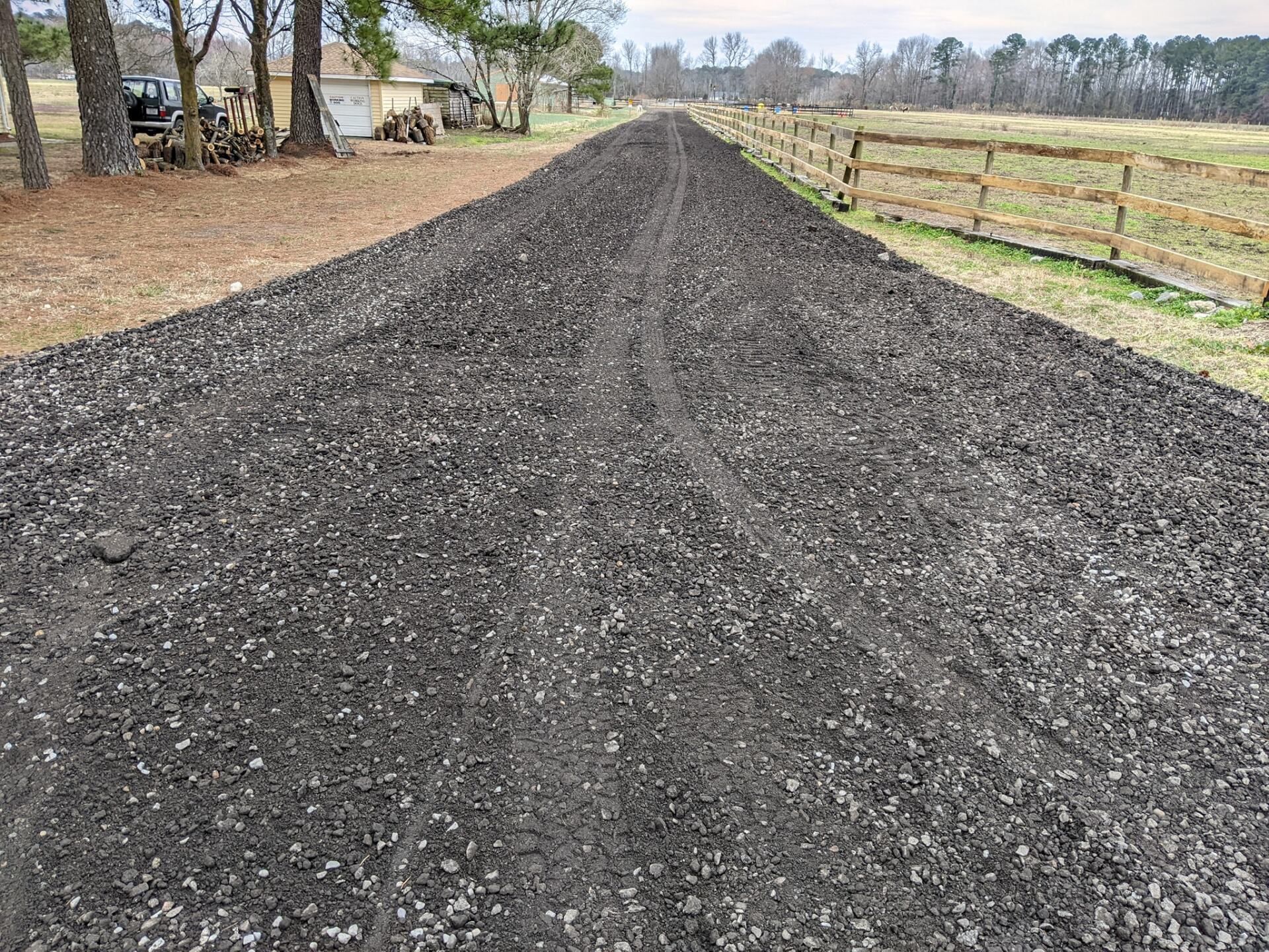 Freshly spread gravel road receding into the distance beside a fenced field and trees