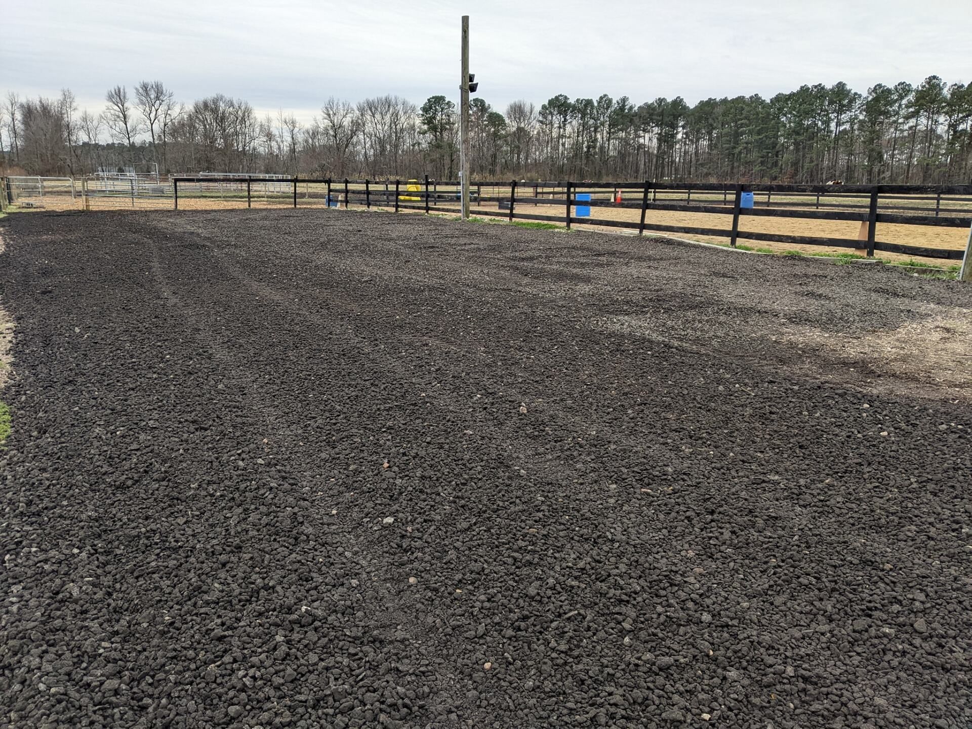 Freshly tilled dark soil field beside a wooden fence under an overcast sky