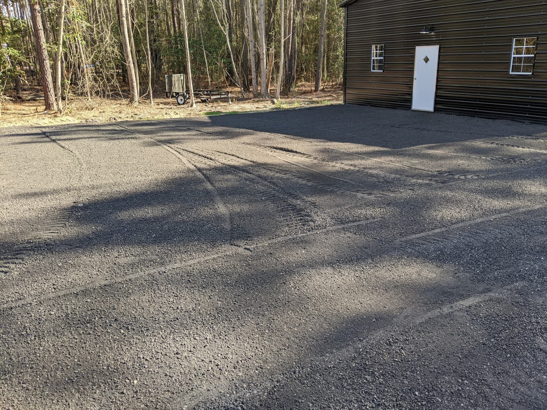 Gravel driveway beside a log cabin and wooded trees, with long shadows across the ground.