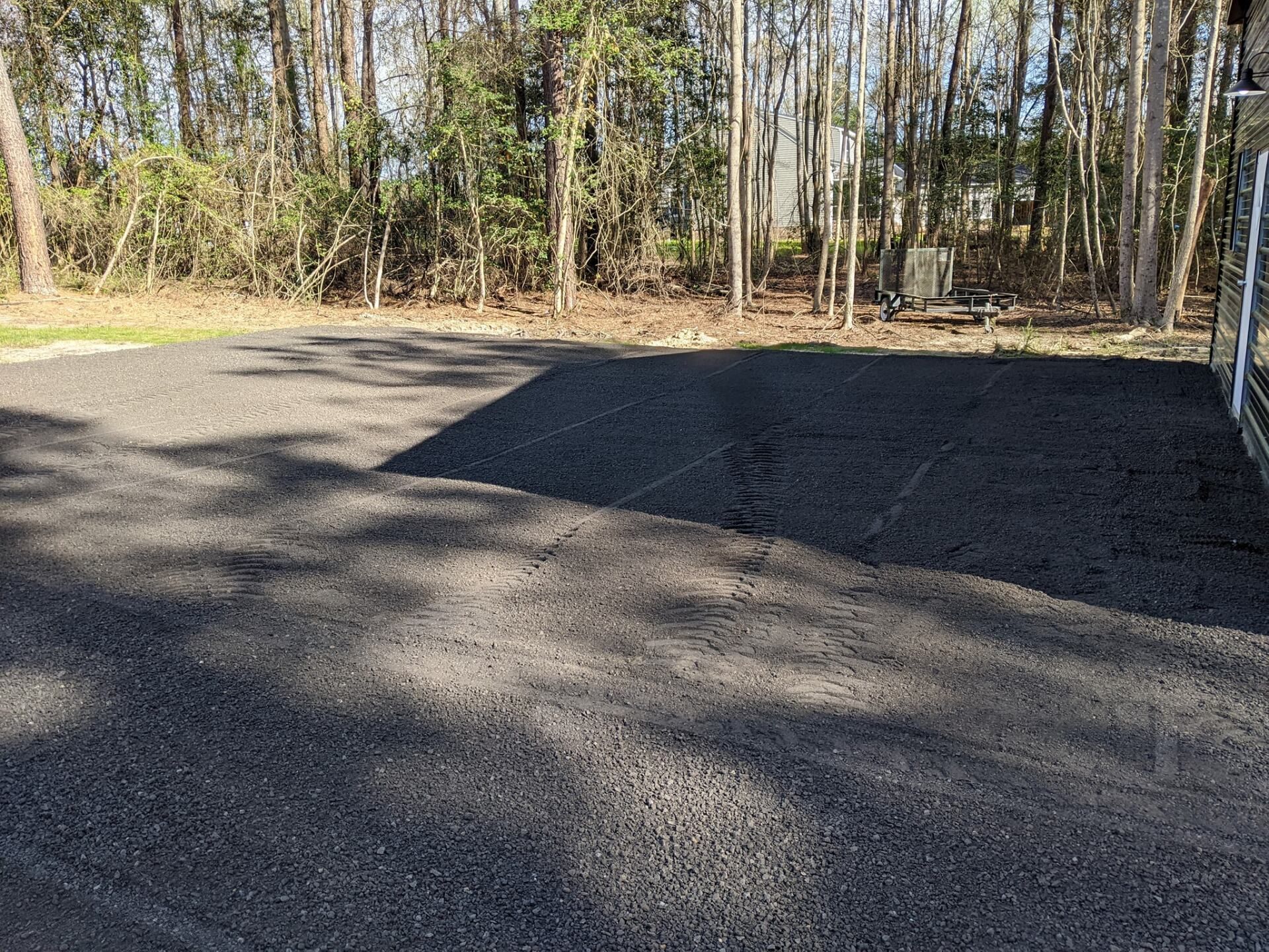 Freshly paved asphalt driveway beside a wooded area in daylight