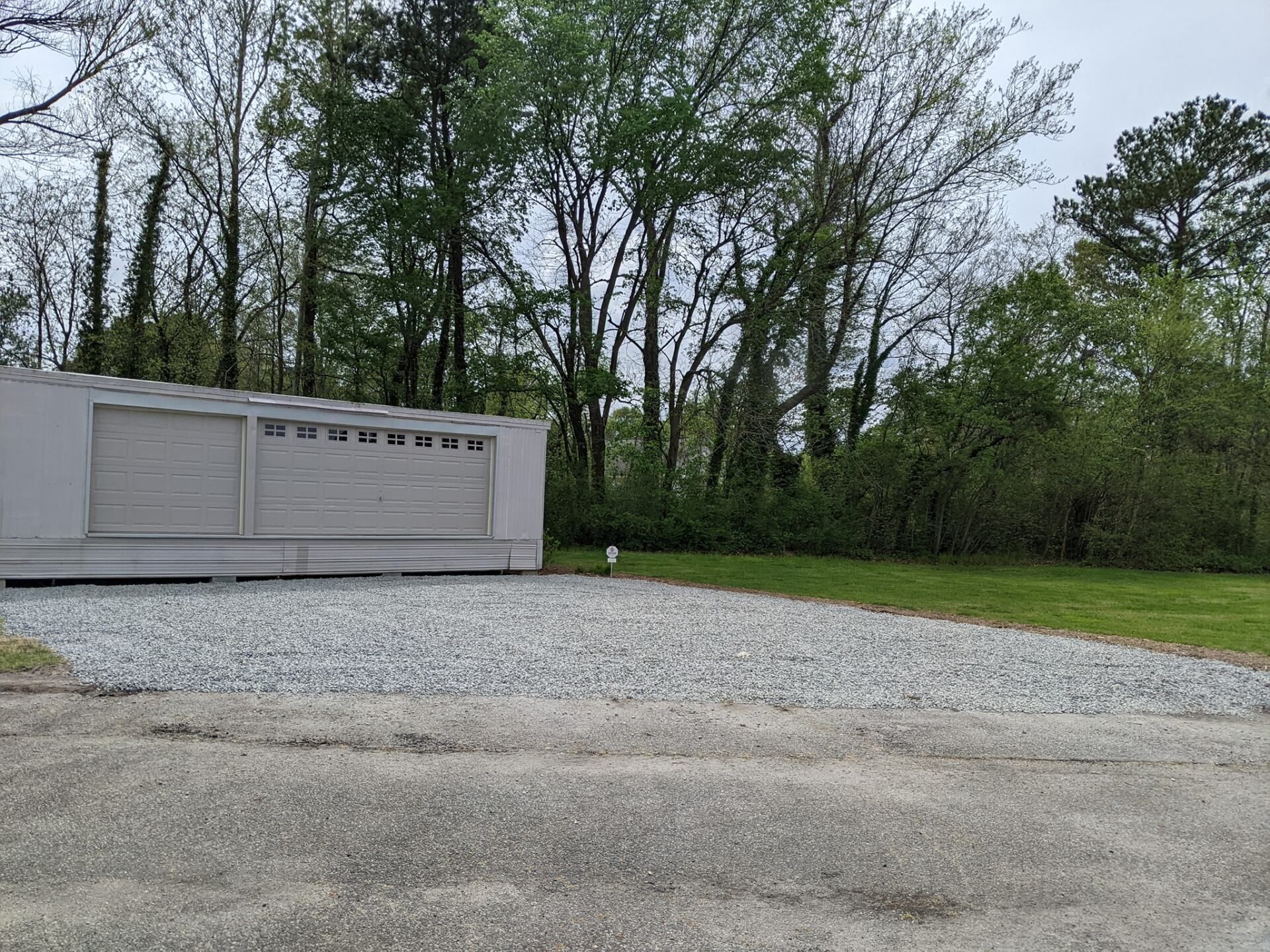 Gray storage shed beside a gravel lot, with trees and grass in the background.