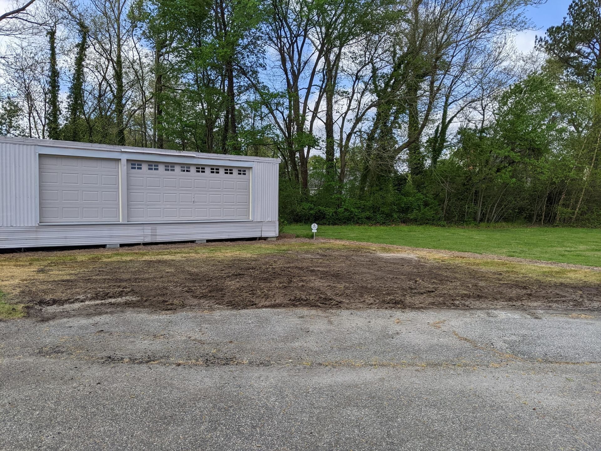 White garage-style shed beside a gravel driveway with trees and grass in the background