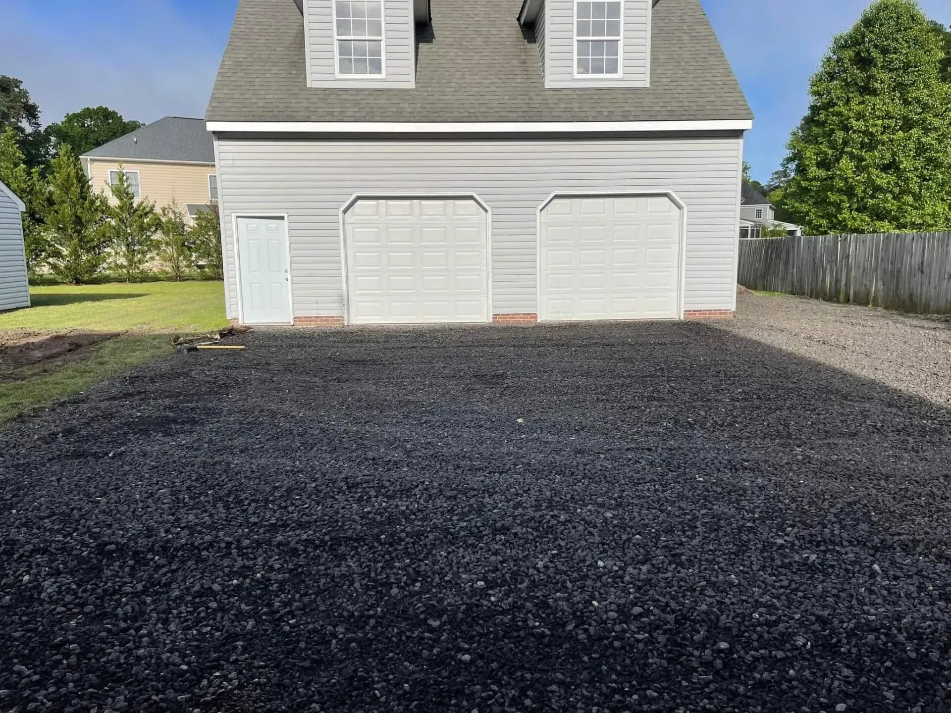 Three-car garage with a newly paved black driveway in front of a gray house