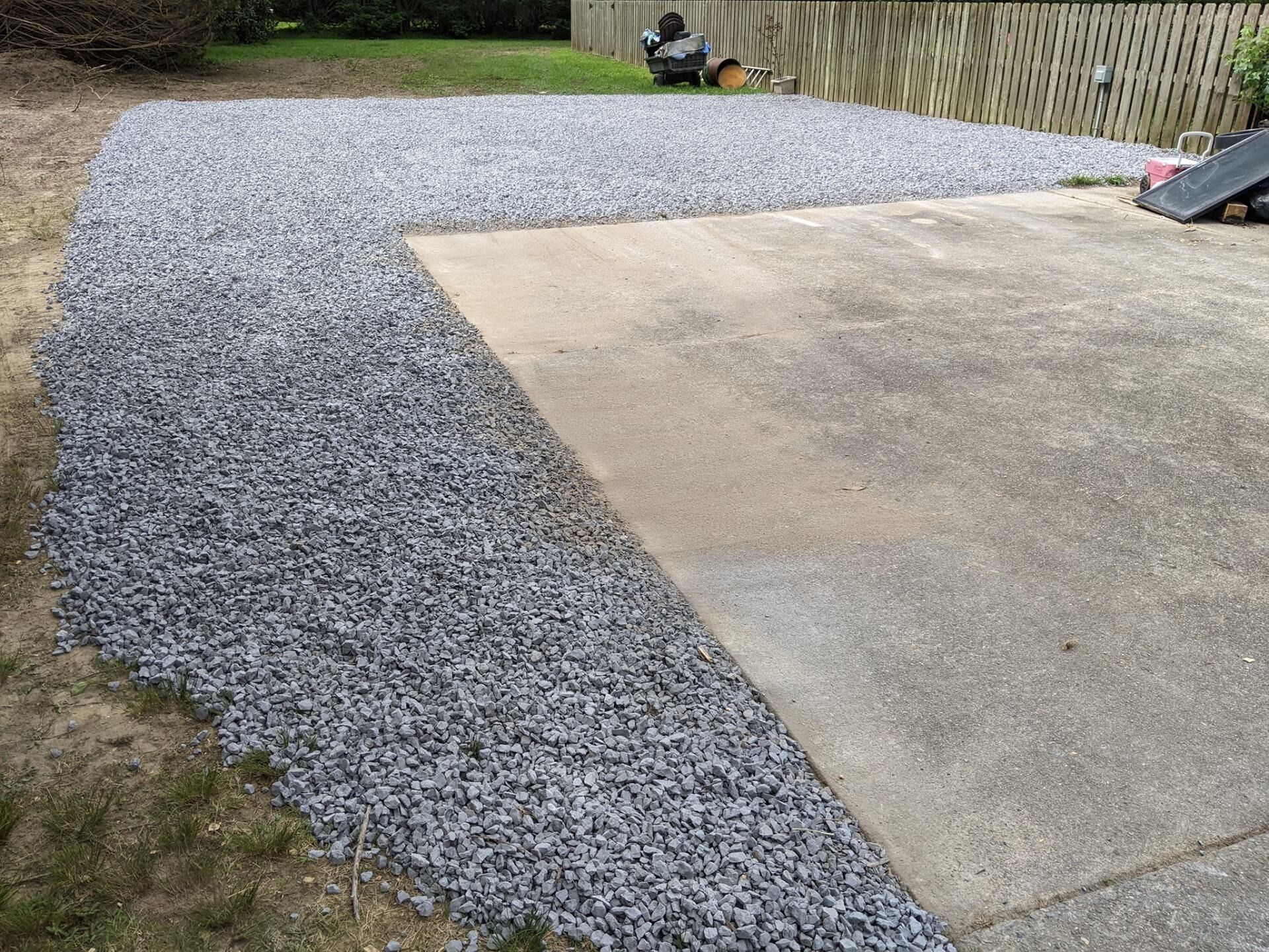 Gravel driveway beside a concrete slab and wooden fence in a backyard