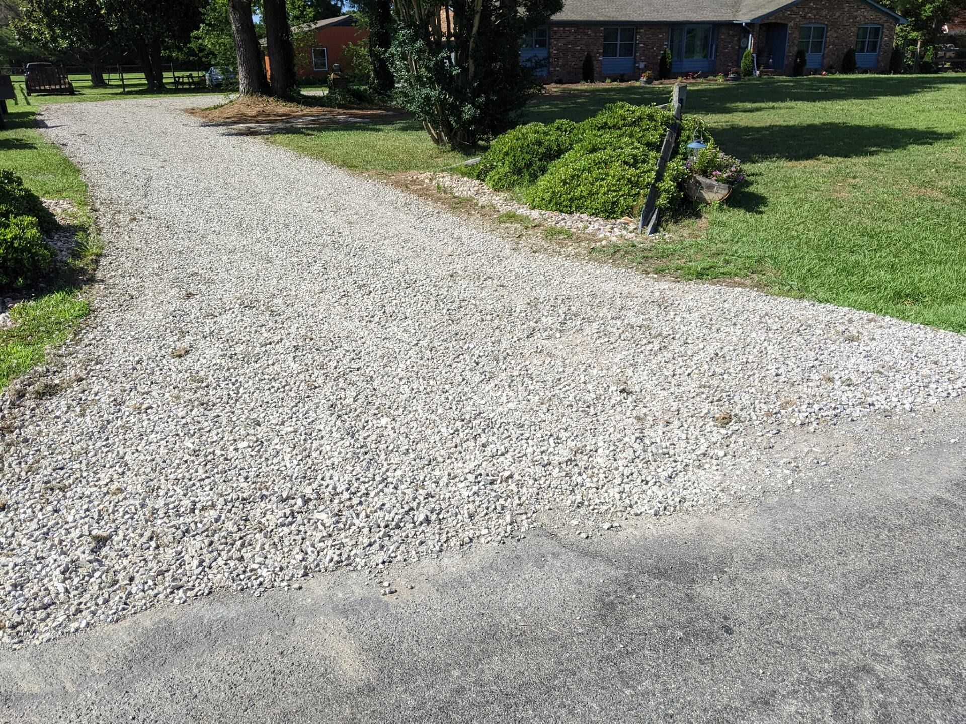 Gravel driveway curving past a grassy yard toward a house in the background.