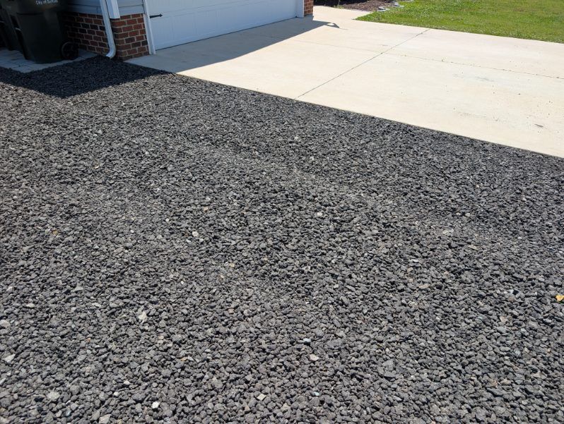 Gravel driveway beside a light-colored concrete garage apron in front of a house