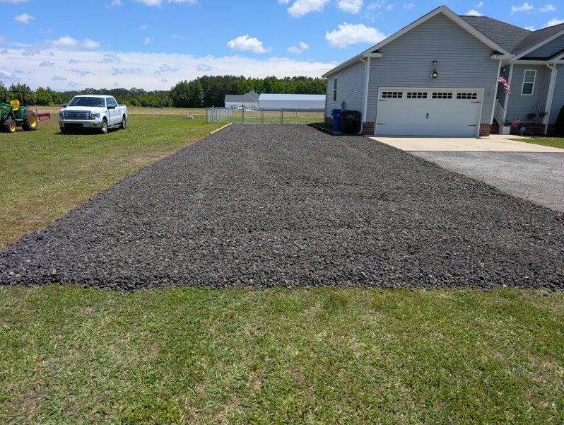 Freshly laid black gravel driveway beside a white house and garage under a blue sky