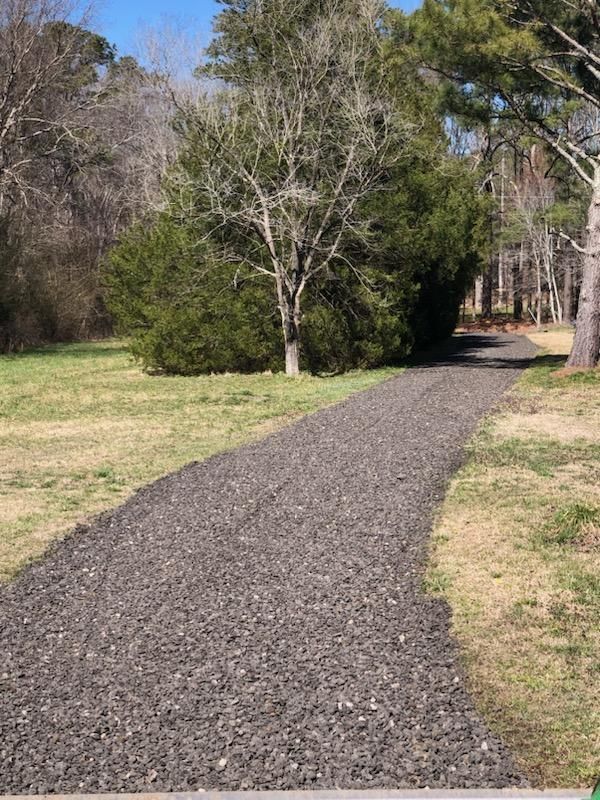 Gravel path curving through a grassy park beside trees under a clear blue sky