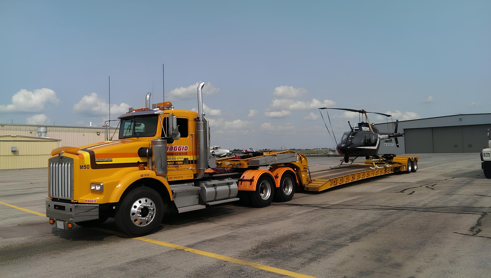 Yellow semi-truck hauling a large green and black bus on a flatbed trailer.