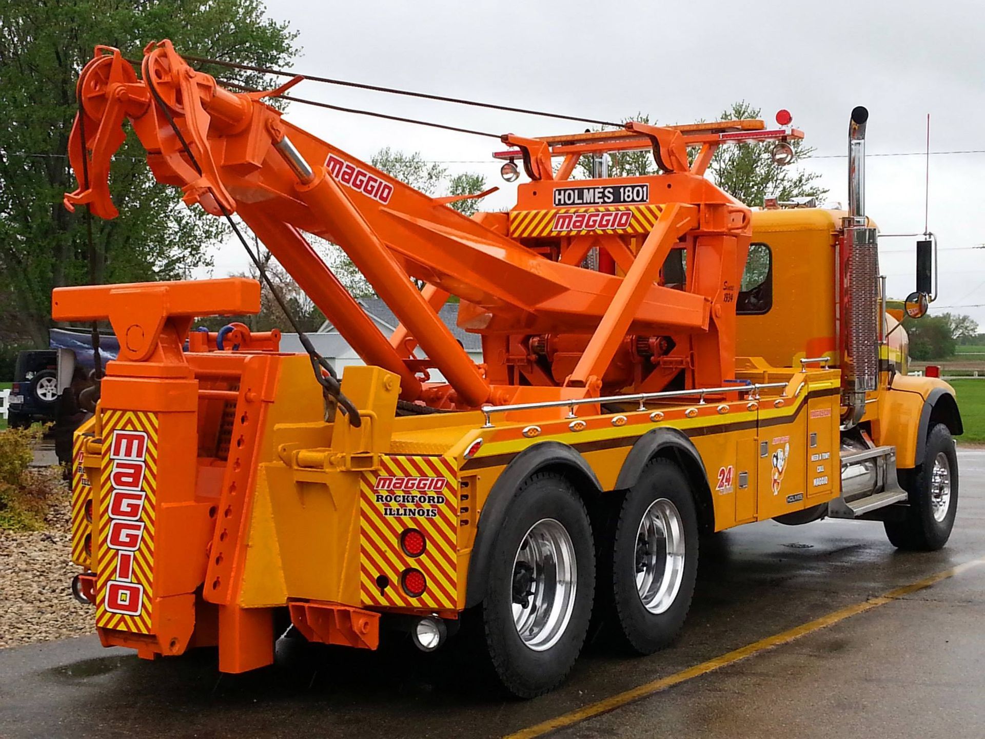 Orange heavy-duty tow truck with extendable boom, parked on a wet road.