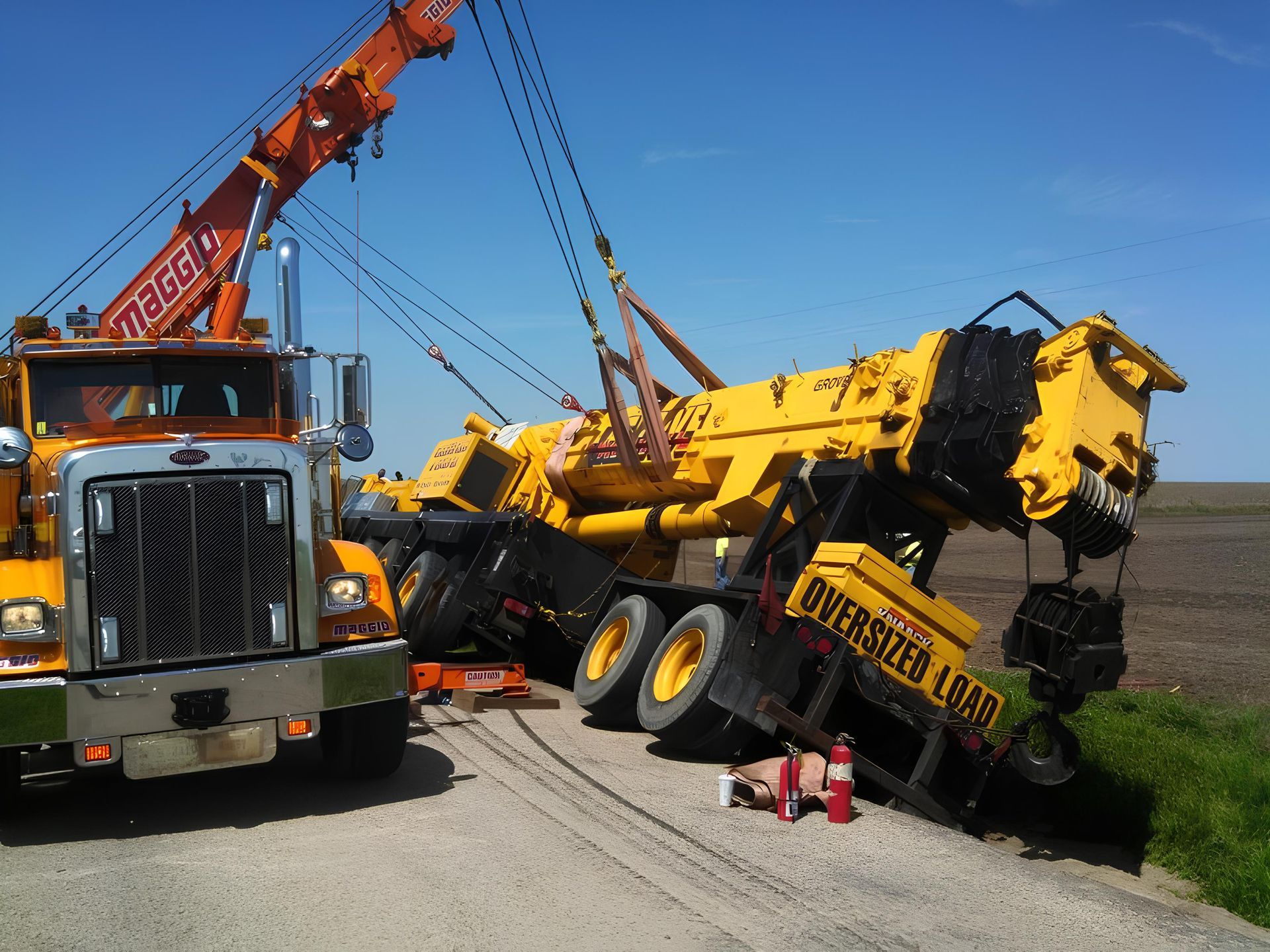 Yellow crane being towed by a tow truck on the side of a road on a sunny day.