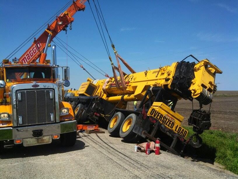 Yellow tow truck righting a tipped-over yellow crane on a roadside. 