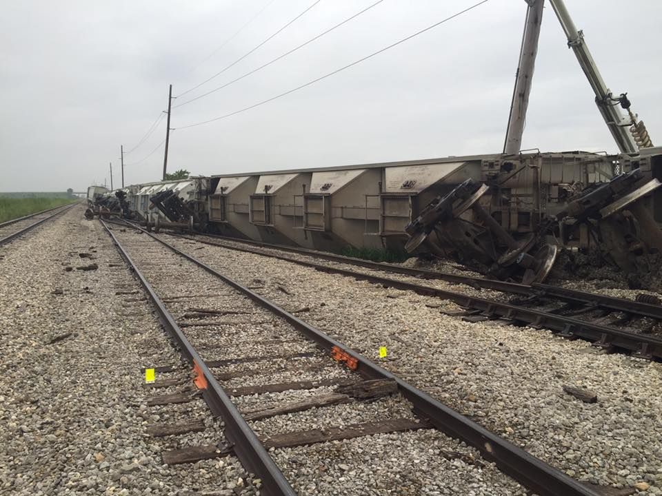 Train derailment, multiple cars overturned on railway tracks. Gray sky, gravel and dirt.