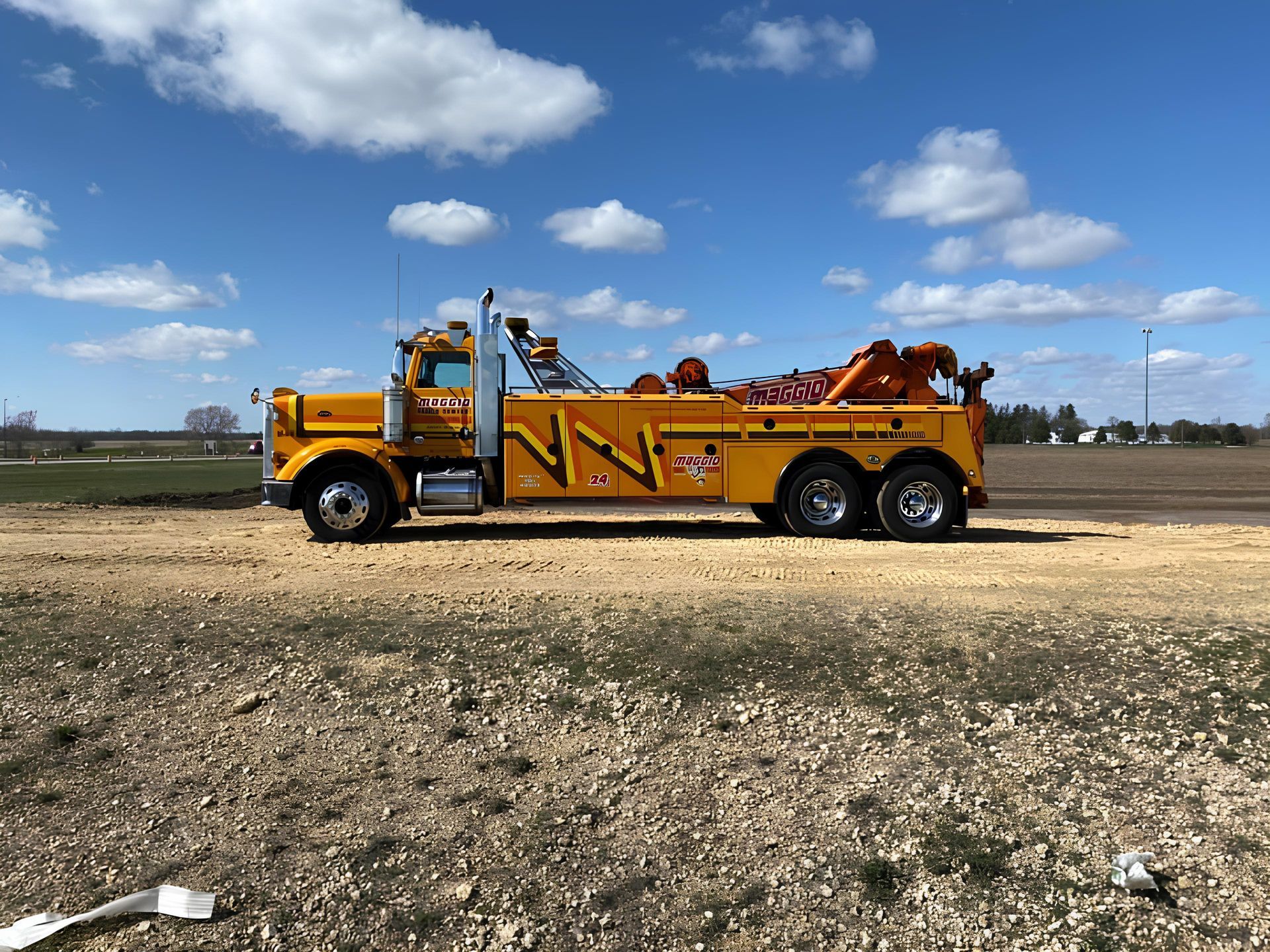 Yellow tow truck on dirt road under a blue sky.