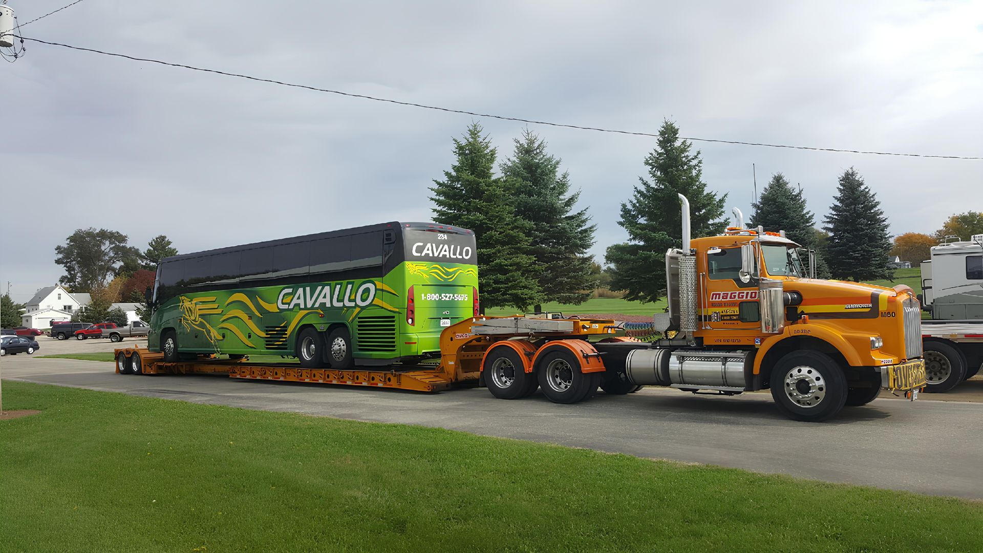 Yellow semi-truck hauling a large green and black bus on a flatbed trailer.