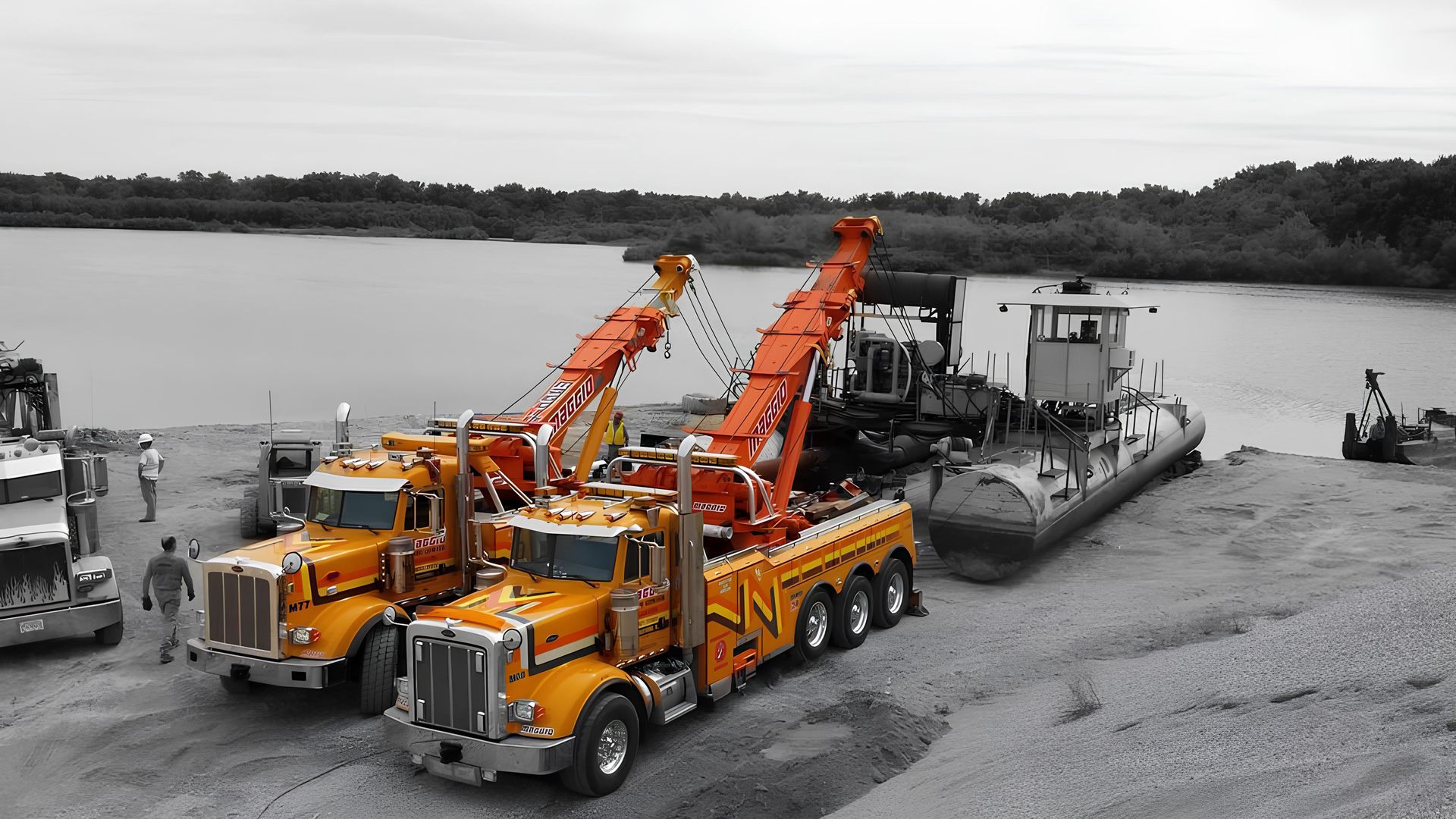Yellow crane overturned on the side of a road, being righted by a tow truck; sunny day.