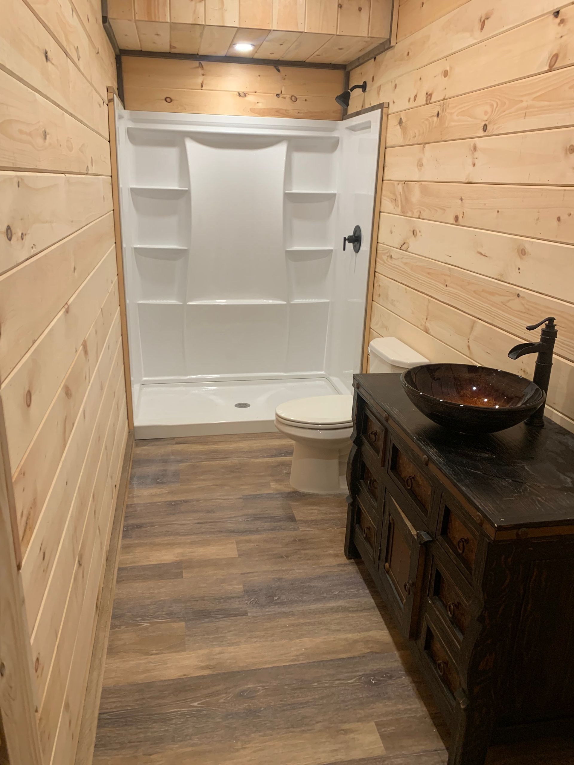 A bathroom with a toilet , sink , shower and wooden walls.