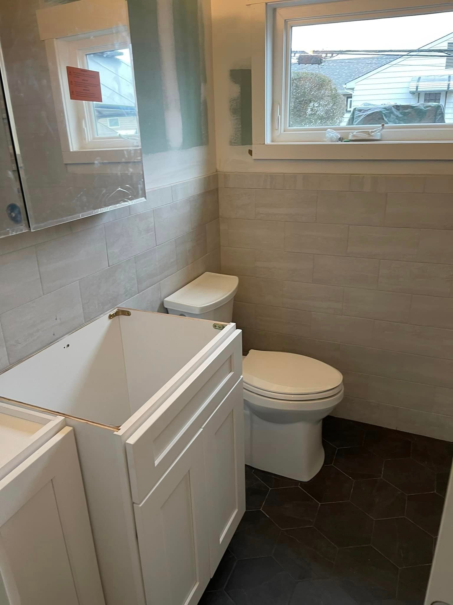 A bathroom with a toilet , sink , mirror and window.
