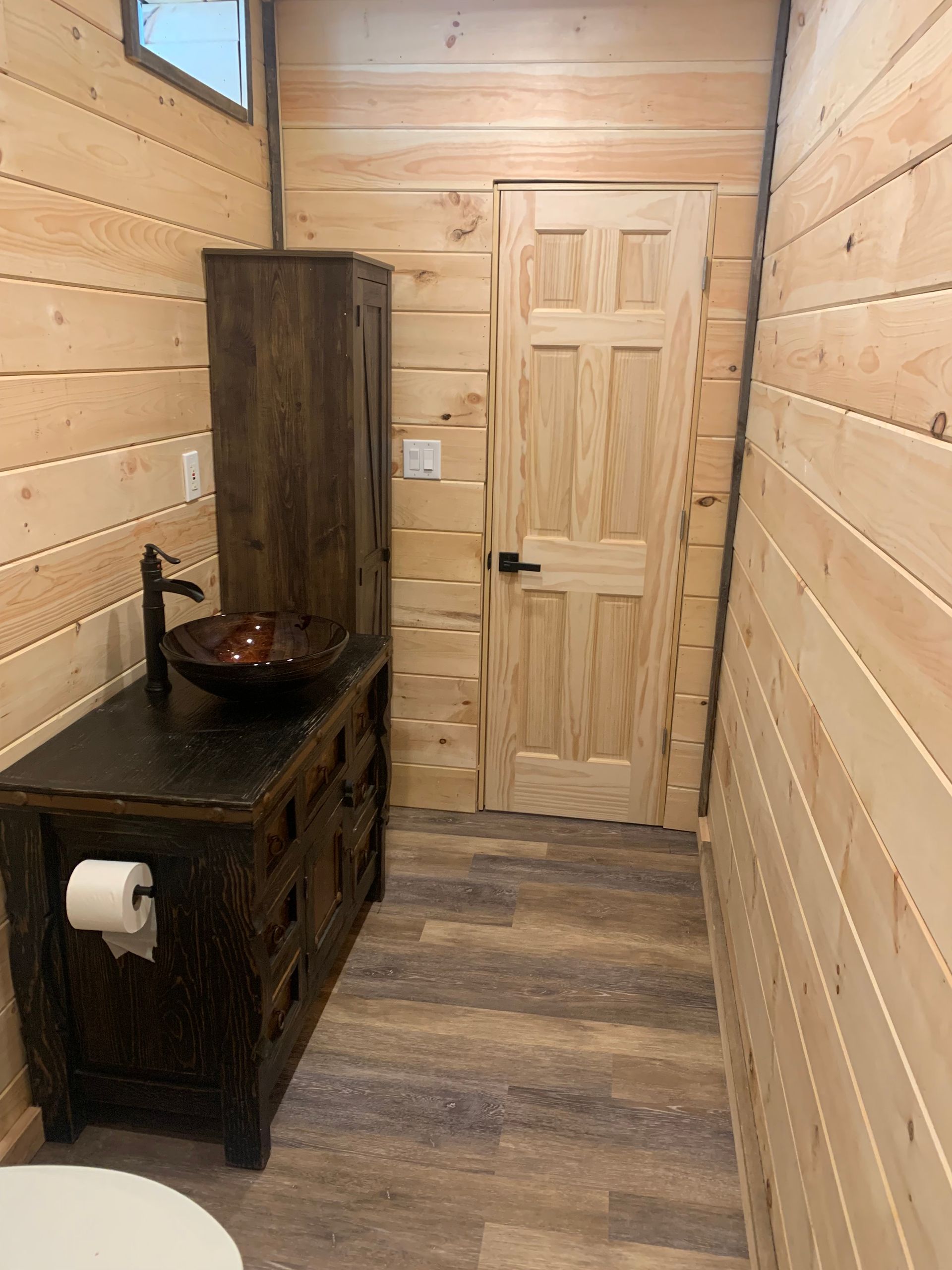 A bathroom with a sink , toilet , cabinet and wooden walls.