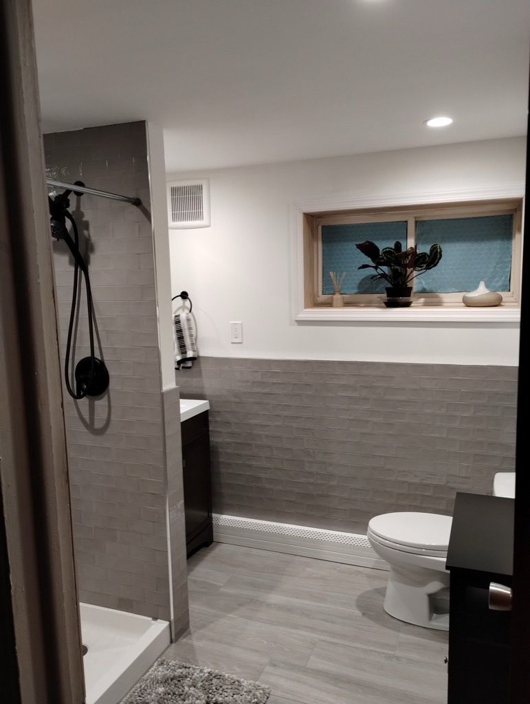 A bathroom with a toilet , sink , shower and window.