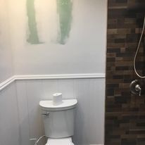 A bathroom with a toilet , shower and a picture on the wall.