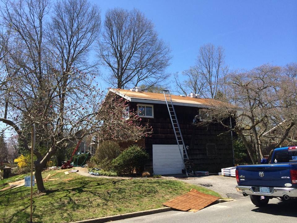 A truck is parked in front of a house with a ladder on the roof.