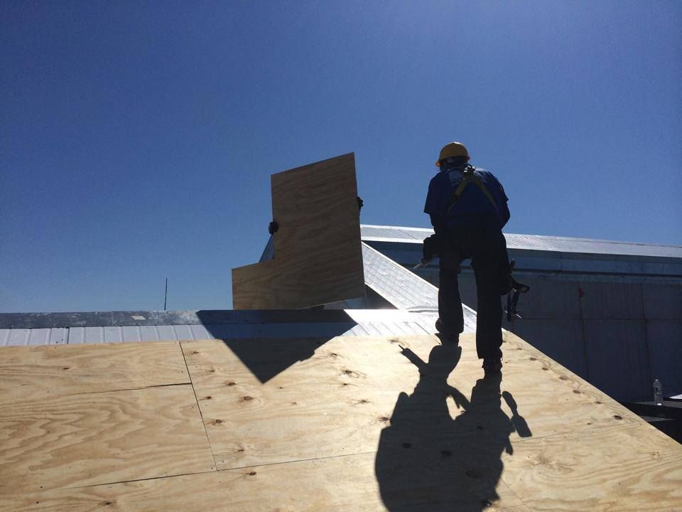 A man is standing on a roof holding a piece of plywood.