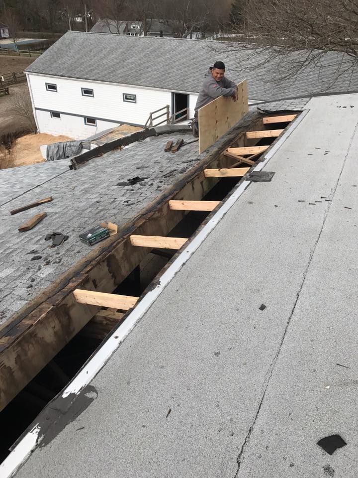 A man is standing on top of a roof holding a piece of wood.