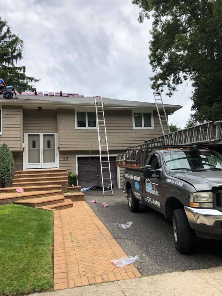 A truck is parked in front of a house with a ladder on the roof.