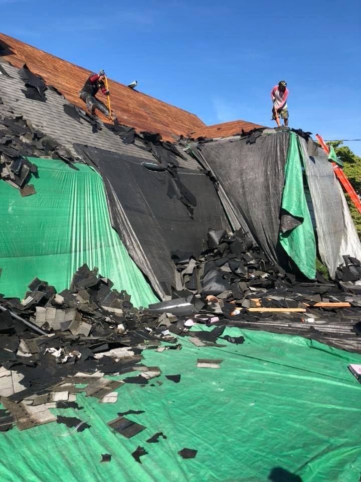 A man is standing on top of a roof with a green tarp covering it.