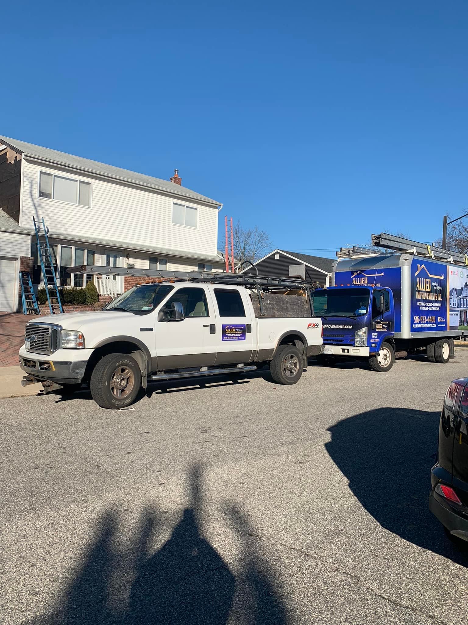 Two trucks are parked in a gravel lot in front of a house.