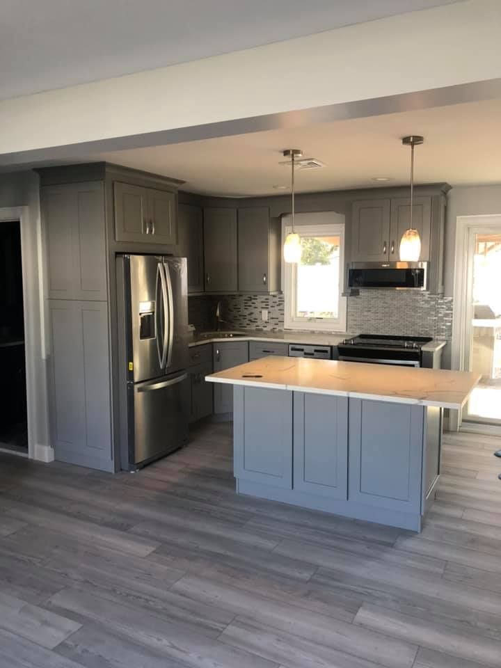 A kitchen with gray cabinets , stainless steel appliances , and a large island.