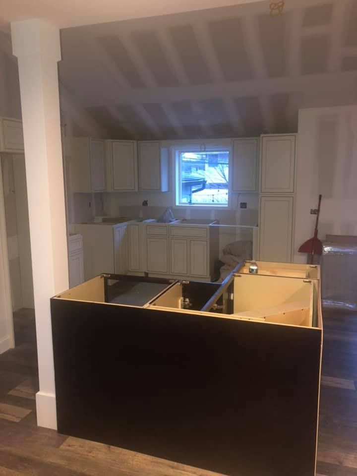 A kitchen under construction with white cabinets and a black island.