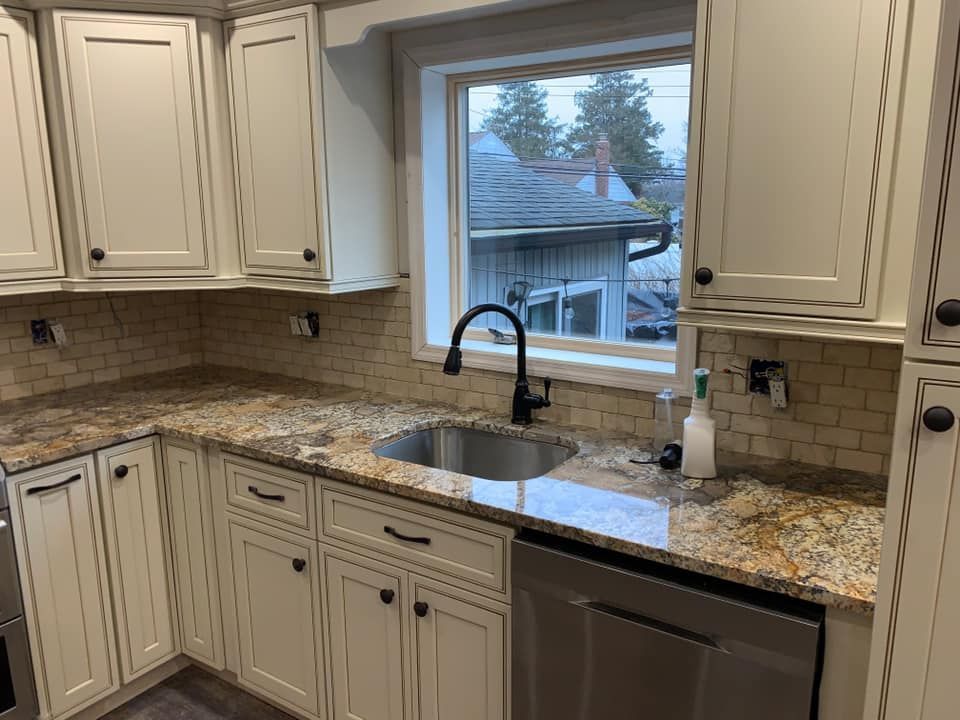 A kitchen with white cabinets , granite counter tops , a sink and a window.