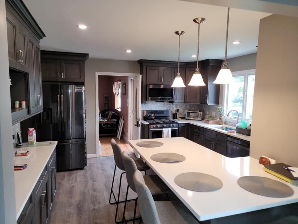 A kitchen with a large island , stools , a refrigerator and a stove.