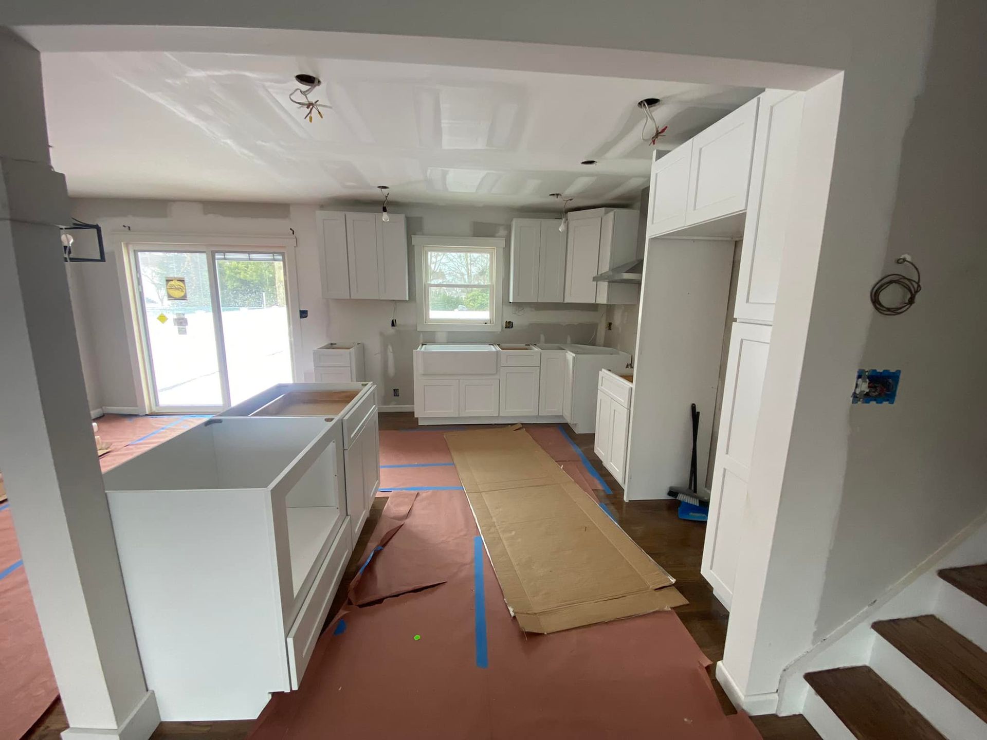A kitchen under construction with white cabinets and stairs.